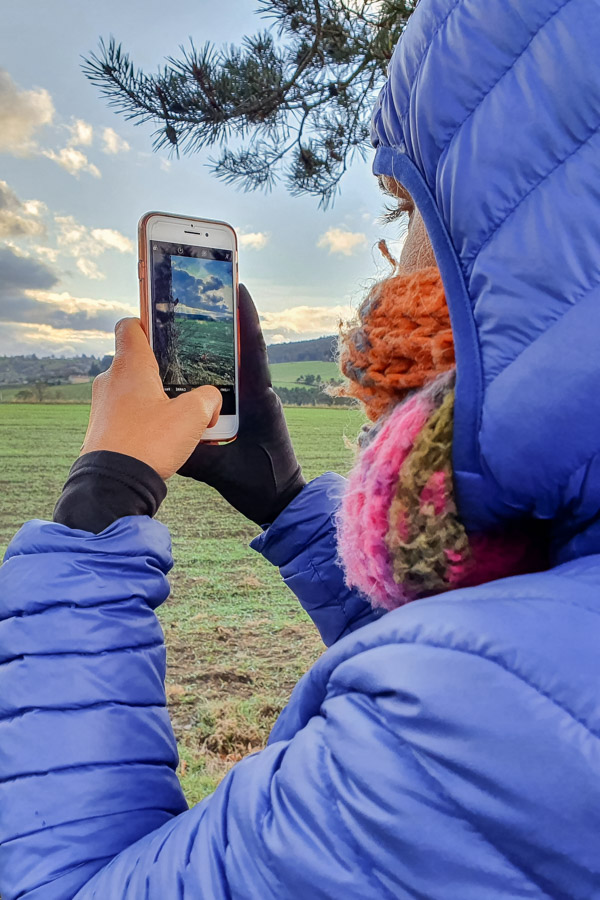 Une femme prend une photo avec son smartphone de la campagne du Parc naturel régional du Pilat, dans la Loire