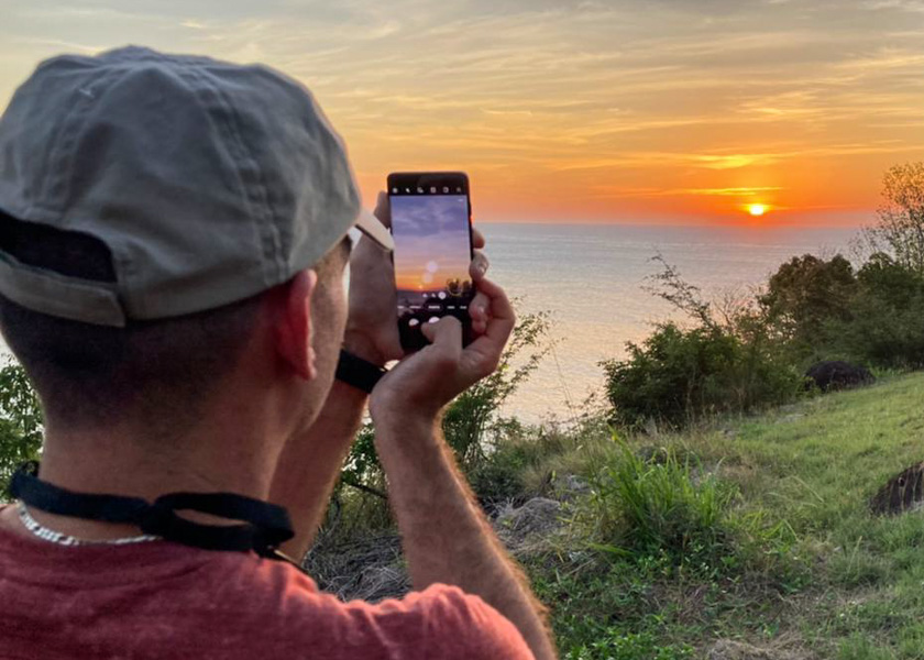 Xavier prend une photo au smartphone d'un coucher de soleil sur l'océan
